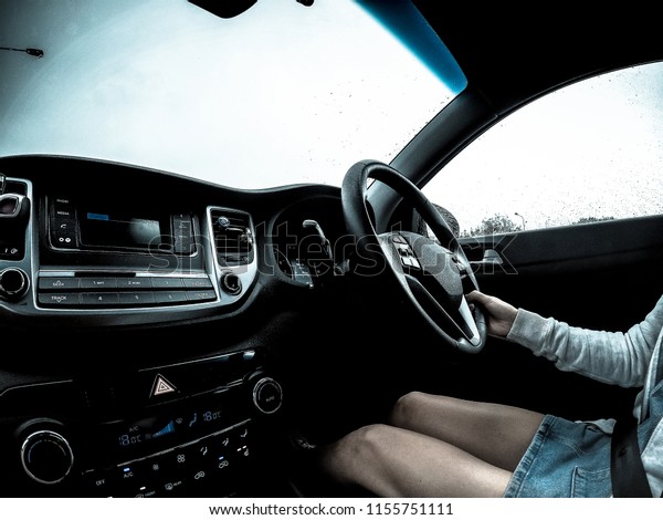 A young\
women in a denim skirt driving on a rainy day, Edited with a cold\
feel, (All trademarks, content\
removed)