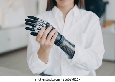 Young women with disability is assembling bionic arm with hand. Cyber sensor hand has processor chip and buttons. European girl adjusting contemporary electronic hand prosthesis at home.