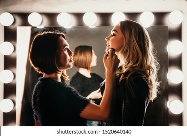 Young women doing makeup , old-fashioned. Stands near mirror. Backstage.