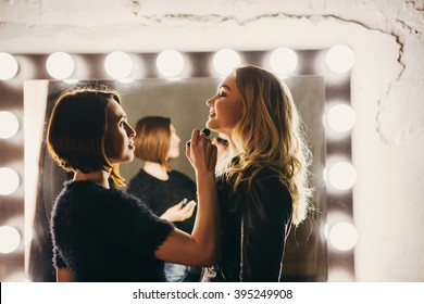  Young Women Doing Makeup , Old-fashioned. Stands Near  Mirror. Backstage.