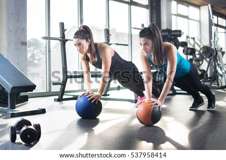 Young women doing stretching exercises on fitness ball in gym.