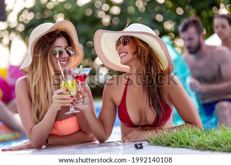 Young women drinking coctail and having fun by swimming pool at hot summer day.