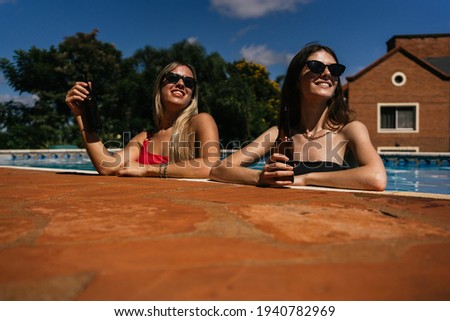 Young women enjoying the swimming pool while drinking beers.