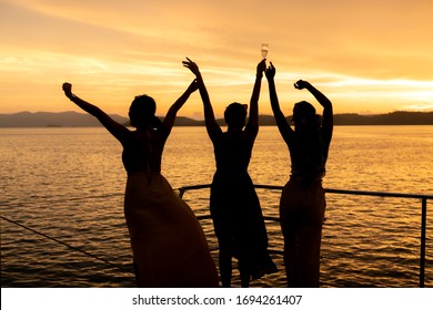 Young women enjoying view of sunset in the ocean while sailing in yacht. One of them hold glass of champaign to celebrate their vacation. Luxury lifestyle and party on yacht background concept.