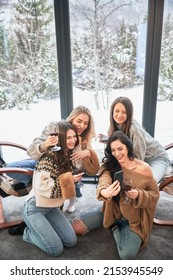 Young Women Enjoying Winter Weekends Inside Contemporary Barn House. Four Girls Having Fun, Taking Selfies On Phone And Drinking Wine.