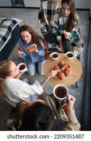 Young Women Enjoying Winter Weekends Inside Contemporary Barn House. Four Girls Having Fun And Eating Croissants And Drinking Hot Tea.