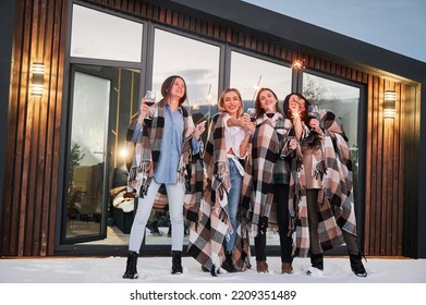 Young Women Enjoying Winter Weekends On Terrace Of Contemporary Barnhouse. Four Girls In Plaids Drinking Wine And Celebrating With Sparklers In The Evening.