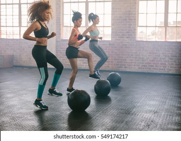 Young women exercising in aerobics class with medicine balls on floor. Three females doing workout together in gym. - Powered by Shutterstock