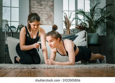 Young women goes in for sports at home, training online. Home workout with a friend, the trainer monitors the plank time on the stopwatch