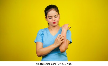 Young women have skin problems, irritation on her skin, skin infection itching red rash, arm scratching with hands, isolated over yellow background