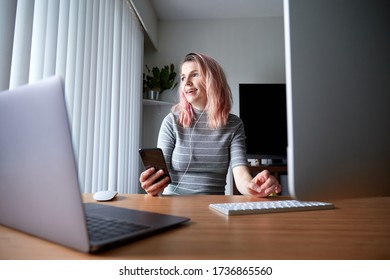 Young Women With Headphones Talking On A Cell Phone With A Slight Smile, In A Home Office Living Room Environment