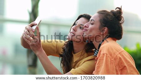 
Young women looking at smartphone device outdoors, candid millennial taking selfie with phone