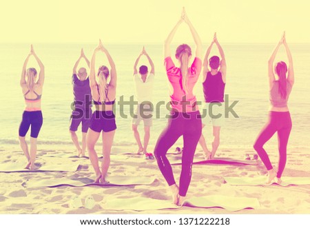 Young women and men exercising yoga poses on sunny beach by ocean