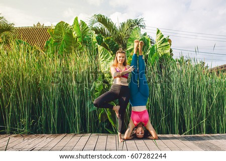 Young women practicing yoga during luxury yoga retreat in Asia, Bali, meditation, relaxation, getting fit, enlightening, green grass jungle background. Acroyoga