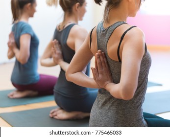 Young women practicing yoga together, they are doing the reverse prayer pose and clasping their hands behind their back
