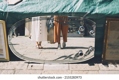 Young women shopping in flea market in Venice. Two girls in clothes made of natural fabrics reflected in antiques mirror. Travel and Vacation in Europe. - Powered by Shutterstock