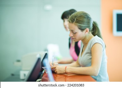 Young Women Signing In At Counter Of Health Club