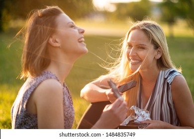 Young women sitting together in park with bars of chocolate - Powered by Shutterstock