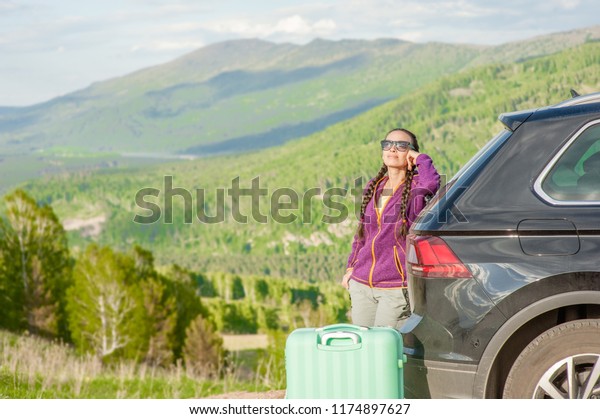 young women with suitcase on summer roadtrip in\
mountains. Space for text
