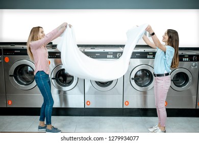 Young Women Throwing Up A Bedsheet Making Clothes After The Washing In The Public Laundry