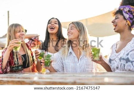 Young women toasting with mojito at chiringuito- Group of fashion girls celebrating bachelorette party while enjoying sunset and drinks on the beach 
