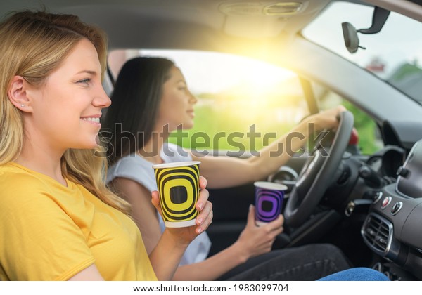 Young women travel by car. Girls in a car drink\
coffee or tea in a good\
mood.