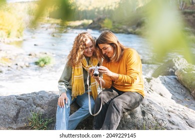Young women travellers friends taking photos on camera on view background of mountains and river, hiking on autumn nature