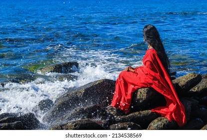 Young Women Wearing A Red Saree On The Beach. Girl In Traditional Indian Sari Among The Rocks And Enjoying The Freedom And The Sunset Or Sunrise. Beautiful Indian Woman On The Beach Wearing A Sari.