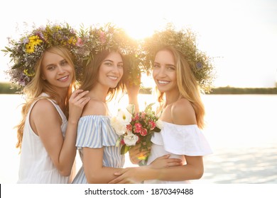 Young women wearing wreaths made of beautiful flowers near river on sunny day - Powered by Shutterstock