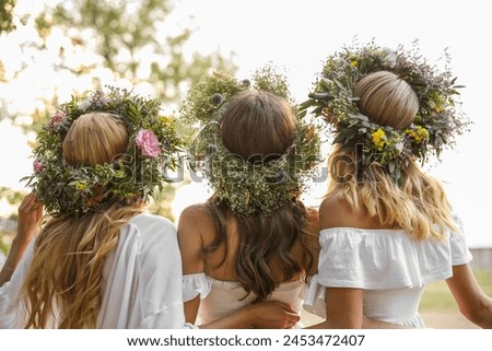 Young women wearing wreaths made of beautiful flowers outdoors on sunny day, back view