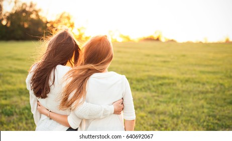 Young women in white sweaters are walking on the green field. Best friends