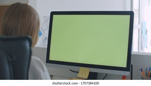 Young Women Work On Computer With Green Mock-up Screen. Girl In Cozy Clothes Sitting In Living Room Using Laptop. Over Shoulder Camera Shot