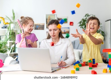 Young women works at home with laptop, along with two children. Children want to communicate with their mother, make noise and interfere with work. Self-isolation during coronovirus pandemic