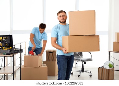 Young Worker With Cardboard Boxes And His Colleague In Office. Moving Service