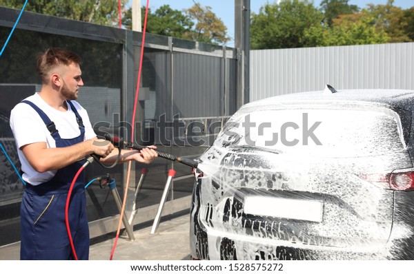 Young worker cleaning automobile with high pressure\
water jet at car wash