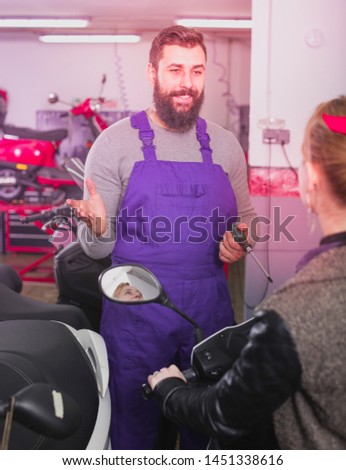 Young worker helping female client to fix bike in motorcycle workshop