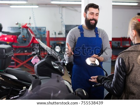 Young worker helping female client to fix bike in motorcycle workshop