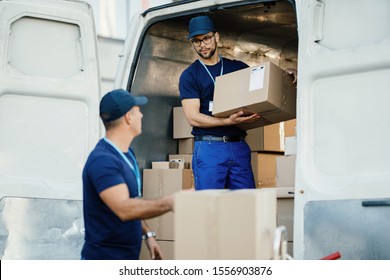 Young worker loading cardboard boxes in a delivery van and communicating with his colleague. 