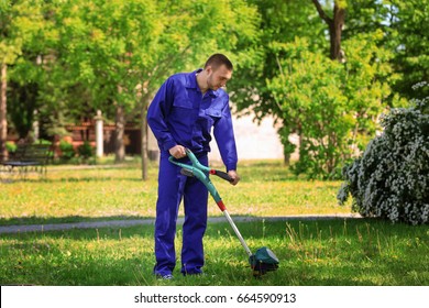 Young Worker Mowing Lawn With Grass Trimmer Outdoors On Sunny Day