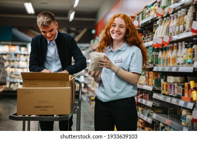 Young worker restocking the shelves with a colleague in the supermarket. Two grocery store employees working together. - Powered by Shutterstock