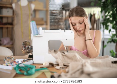 Young worker of the sewing workshop sits tired near the sewing machine, she is overtired