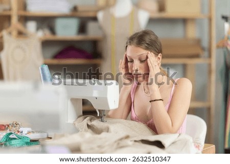 Young worker of the sewing workshop sits tired near the sewing machine, she is overtired