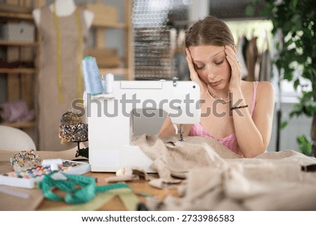 Young worker of the sewing workshop sits tired near the sewing machine, she is overtired