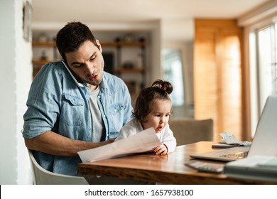 Young working father babysitting his small daughter and making a phone call at home. 