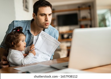 Young Working Father Using Laptop While Babysitting His Small Daughter At Home. 