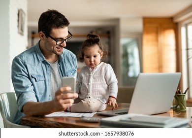 Young working father using mobile phone and communicating with his small daughter at home. 
