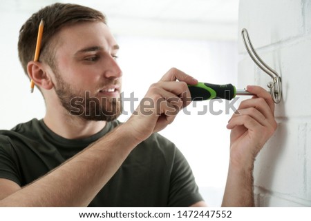 Young working man fixing clothes hook on wall at home