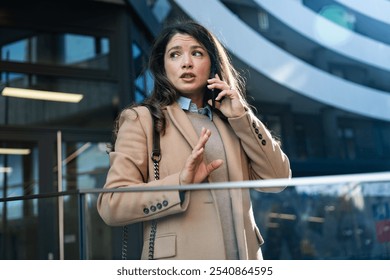 Young worried stressed businesswoman talking on the smart phone outside of office building, having problems on the work place. Business female having conversation with employee colleagues on telephone - Powered by Shutterstock