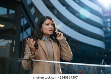 Young worried stressed businesswoman talking on the smart phone outside of office building, having problems on the work place. Business female having conversation with employee colleagues on telephone - Powered by Shutterstock