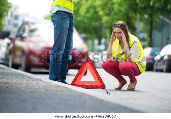 Young Worried Woman Crouching Near\
Triangular Warning Sign With Broken Down Car On\
Street